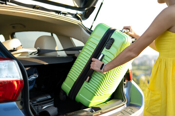 Close up of woman taking green suitcase from car trunk. Travel and vacations concept.