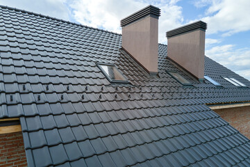 Closeup of attic windows and brick chimneys on house roof top covered with ceramic shingles. Tiled...