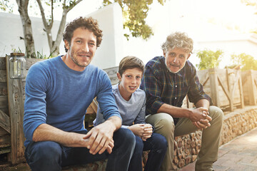 Family is everything. Portrait of a young boy sitting with his father and grandfather in their backyard.