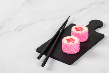 Sweet round sushi with red jelly flower sakura, sprinkled with coconut shavings on a serving board....