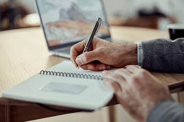 Man writing in spiral notebook and using laptop