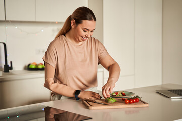 Lovely woman chef with artificial limb preparing breakfast while standing at the light kitchen