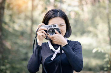 Portrait of a nature photographer covering her face with the camera green forest background.