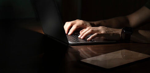 Cropped shot of businessman working on Laptop at desk. Dark tone with copy space.