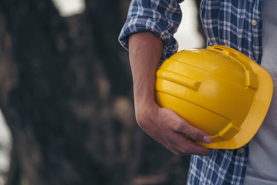 Engineer Man Hands Holding Hardhat White Work Helmet Hard Hat For Civil Construction Engineering. Construction Engineer Man In Safety Suit Hold White Work Helmet Hard Hat On Hands At Construction Site