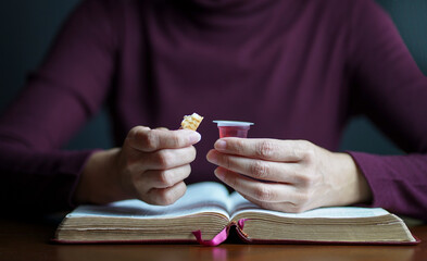 Woman holding biscuit and cup of wine with an open Bible on top of table, Taking Christian Holy Communion concept.