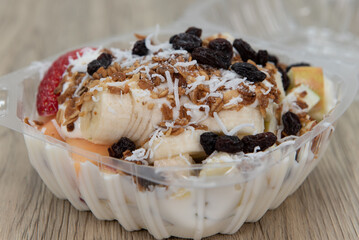 Delicious and healthy fruit bowl snack with banana, raisins coconut, and yogurt all served in a take out order carton