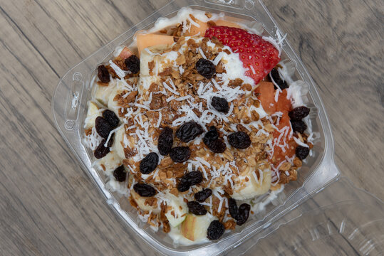 Overhead view of delicious and healthy fruit bowl snack with banana, raisins coconut, and yogurt all served in a take out order carton
