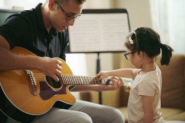 Scene of toddler exploring music instrument, Adorable little girl with music teacher playing guitar while she is experiment the sound of Guitar Strings. kid brains developments. Back to school.