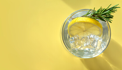 Top view of lemonade with ice cubes in drinking glass on yellow