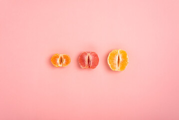 tangerine, grapefruit and orange cut in half on a peach background as a symbol of the vagina and female fertility - obrazy, fototapety, plakaty