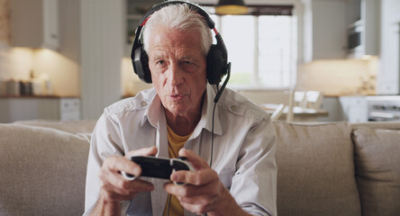 Ooo, the opponents getting close. Shot of a senior man sitting alone on the sofa at home and wearing headsets while gaming.