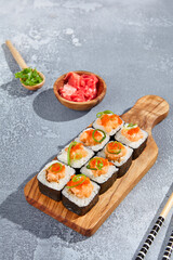 Maki roll with salmon tartare top and tobiko on wooden board in contemporary composition. Sushi roll with chopsticks on concrete table. Maki sushi in minimal style.