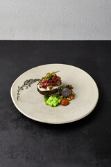 Beef tartare on rye bread with capers, cucumbers, cheese espuma and spices. Meat tartare on handmade ceramic plate. Innovative recipes on modern dishware.