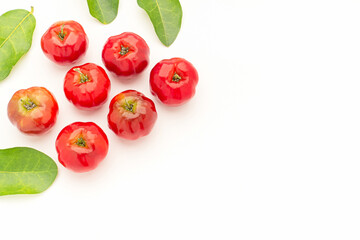 Pile of ripe red acerola cherries and green leaves on a white background