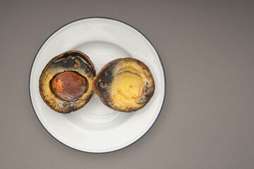 Rotten avocados cut in half on a white dish over a gray background