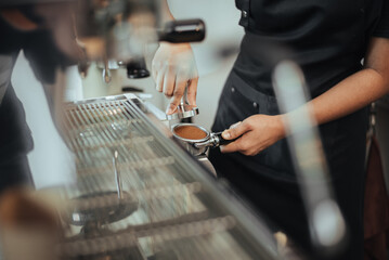 Barista using a tamper to press ground coffee into a portafilter. Close-up view on barista hands to making coffee with coffee machine. Coffee owner concept.