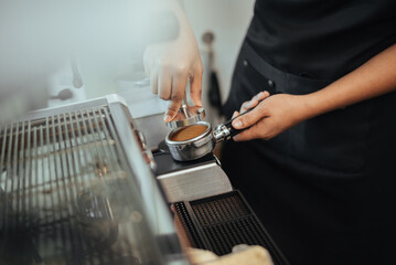 Barista using a tamper to press ground coffee into a portafilter. Close-up view on barista hands to making coffee with coffee machine. Coffee owner concept.