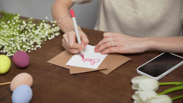 Close-up on a table with items to create a composition for Easter. A woman's hand writes with a red marker: Easter menu. Christ is risen. Church holiday-Easter