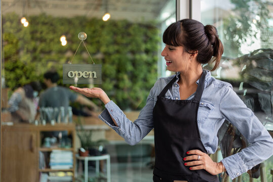 Portrait Of Happy Woman Coffee Owner Standing And Smiling At Her Restaurant Gate With Open Signboard. Business Woman Standing At Cafeteria Door Entrance. Business Owner Concept.