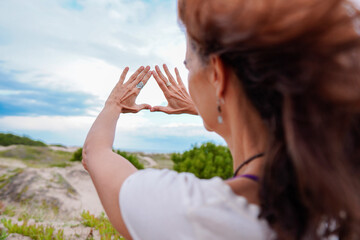 Latin female in the dunes is receiving the spring season by making a symbol of gratitude with her hands looking up the clouds in the sky and breathing fresh air. Freedom and joyful lifestyle concept.