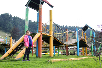 Latin little girl with long straight black hair, overweight body positive and does sports playing in the playground in the middle of the forest and mountains with trees
 - obrazy, fototapety, plakaty