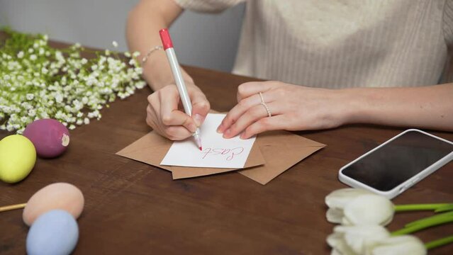 Close-up on a table with items to create a composition for Easter. A woman's hand writes with a red marker: Easter menu. Christ is risen. Church holiday-Easter