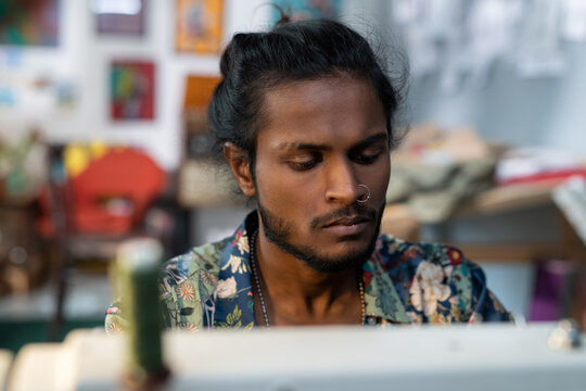Young contemporary designer of clothes sitting in front of electric sewing machine and working over new fashion collection