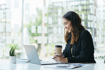 Fototapeta premium Happy young indian business woman entrepreneur using computer looking at screen working in internet sit at office desk, smiling hindu female professional employee typing email on laptop at workplace