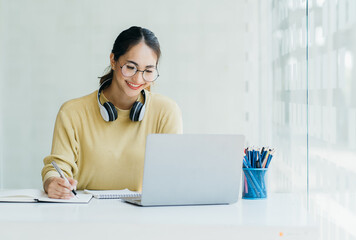 Portraits of beautiful smiling Asian women relax using laptop computer technology while sitting on their desks and using their creativity to work, work from home concept.