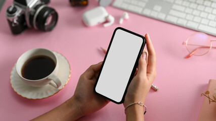 Female hands holding smartphone over her stylish pink office desk.