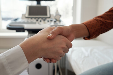 Handshake of young clinician and patient against ultrasound equipment and medical couch in office of contemporary clinics