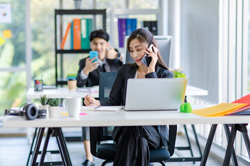 Asian young happy pretty female businesswoman employee staff in formal suit sitting smiling talking on smartphone call working consulting discussing with customer at working desk with laptop computer