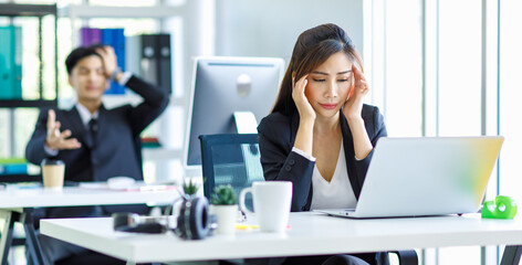 Fototapeta na wymiar Asian young stressed depressed tired exhausted female businesswoman employee staff in formal suit sitting holding hands at head having problem migraine headache same as businessman colleague behind