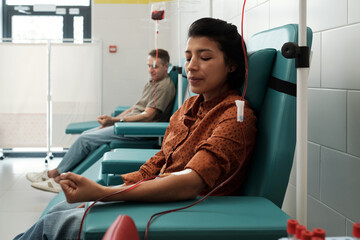 Young female and mature male donors giving blood for sick patients of modern hospital while sitting...