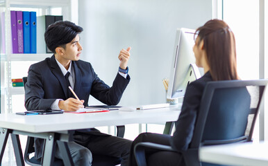 Asian young professional male businessman human resource manager in formal suit sitting at working desk taking note on clipboard interviewing unrecognizable unknown female businesswoman applicant