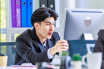 Naklejka premium Closeup shot of Asian young angry crazy mad upset unhappy male businessman employee staff in formal suit sitting at working desk holding hands on computer screen monitor shouting yelling aggressively
