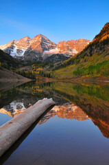 A log on Maroon Lake below the dawn-lit Maroon Bells, Aspen, Colorado, USA
