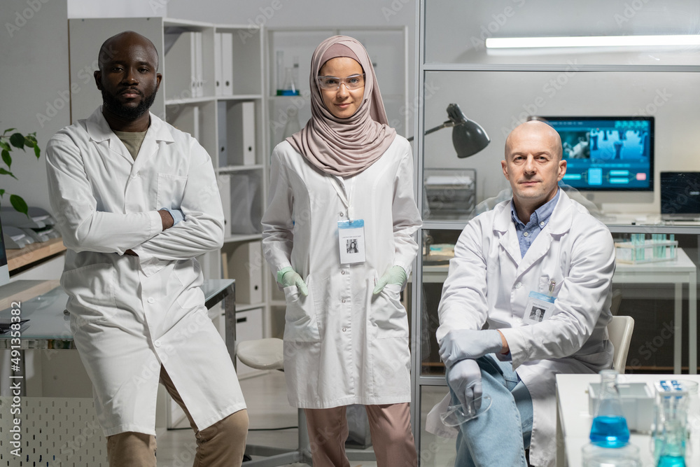 Aufkleber group of three interracial microbiologists in lab coats sitting by workplace in clinical or scientif