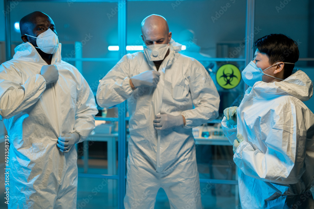 Aufkleber Group of interracial scientists putting on biohazard suits while standing in front of laboratory to work with dangerous substances