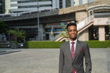 Portrait of handsome young African businessman outdoors in city