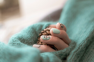 Knitted material around a manicured hand. Green rustic pattern, young female fingers with colorful nail design. Selective focus on the details, blurred background.