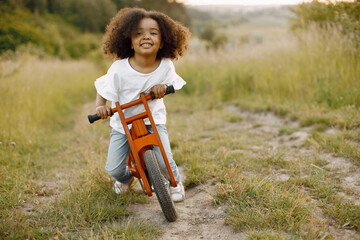 Little african girl is riding a balance bike in the spring park