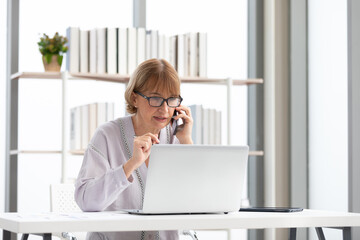 senior businesswoman or freelance using laptop computer and talking about work on phone