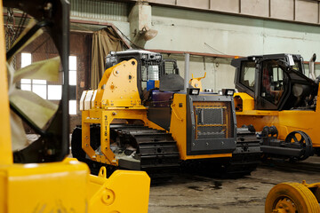 Group of huge road construction machines with caterpillar tyres standing inside large warehouse or garage of modern factory