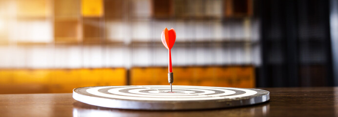 Red dart arrow hitting in the target center of dartboard on bullseye with sun light vintage style,...