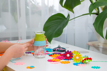 The child's hands wrap yarn around a glass jar, for making crafts at home. With my own hands.