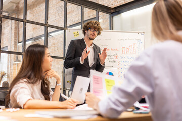 A cheerful young business team, Caucasian and Asian, man and women standing around table, brainstorming about work on table.. Meeting of business partners at the conference on business development