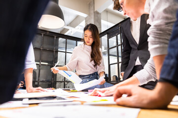 A cheerful young business team, Caucasian and Asian, man and women standing around table, brainstorming about work on table.. Meeting of business partners at the conference.