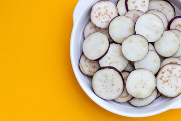 Fresh eggplant in bowl on yellow background.